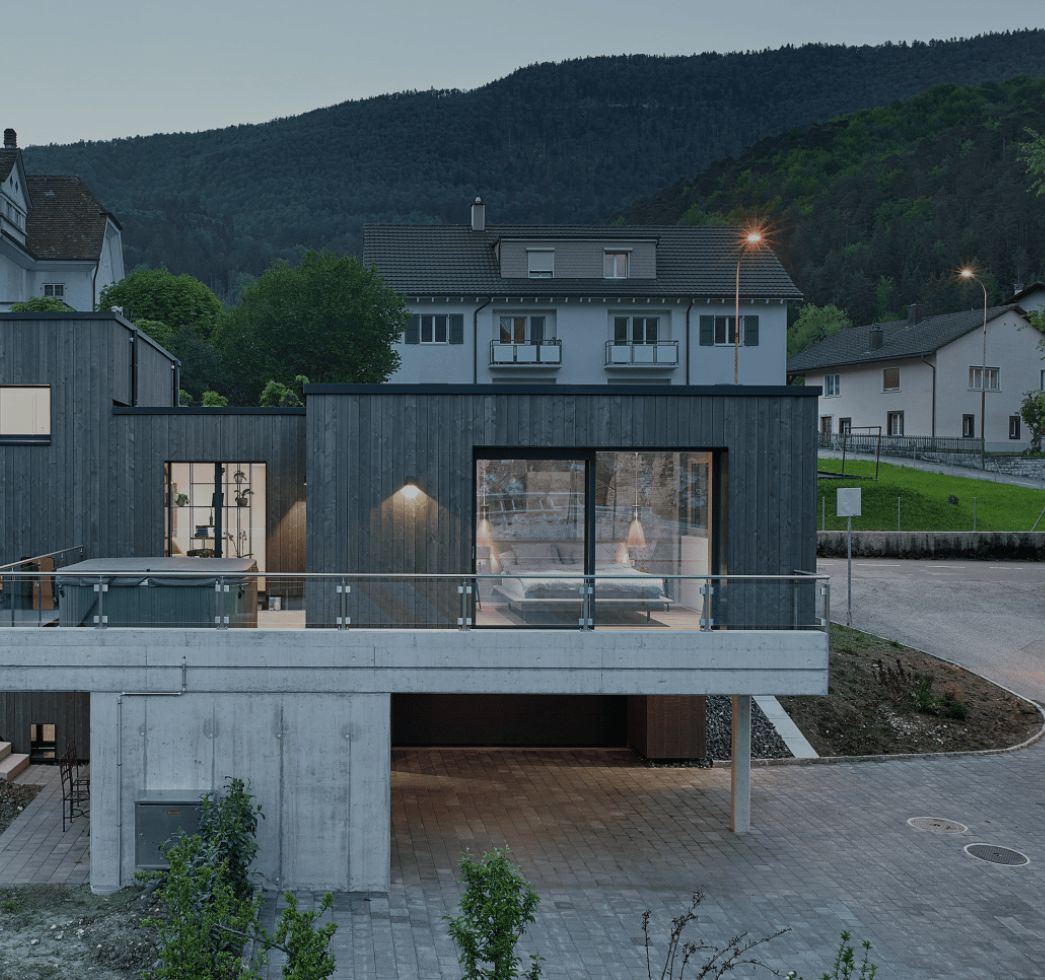 Maison en bardage bois sombre au crépuscule, terrasse sur socle en béton
